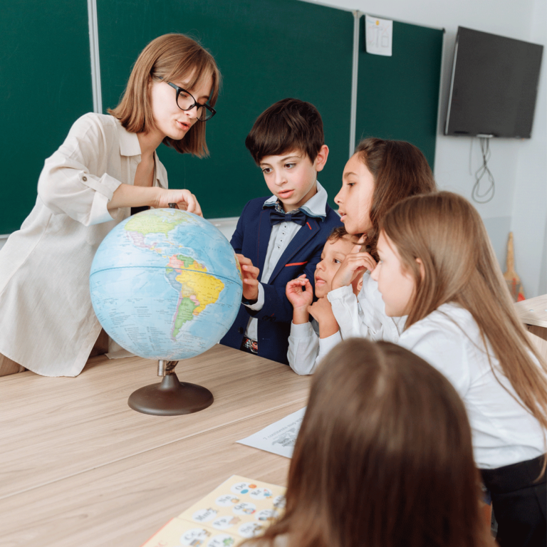 Geography teacher pointing to countries on a globe with young school children watching